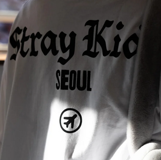 White sweatshirt with 'Stray Kids SEOUL' text and airplane icon on a blurred background