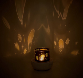 Candle in a holder with star and moon projections on a dark background